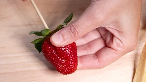 hand skewers strawberry on wooden stick