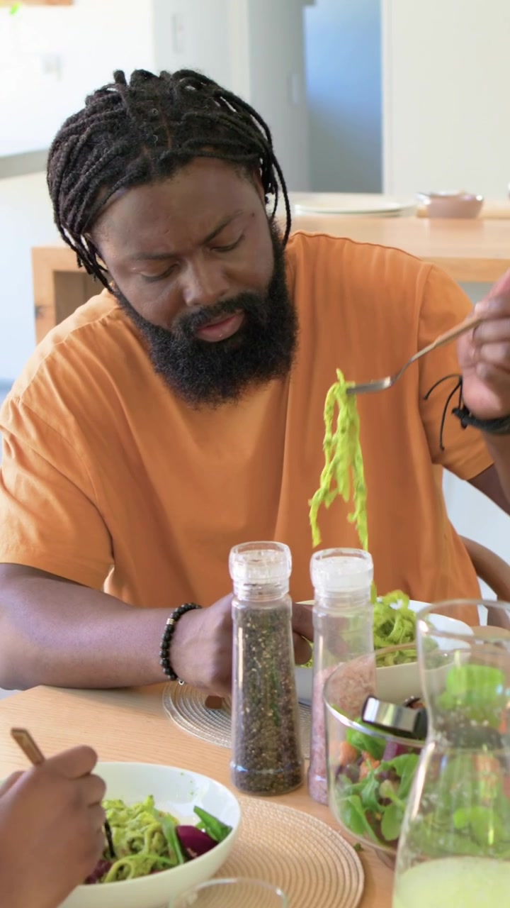 Vertical video: Reaching bowl man orange T seasoning noodles with chopsticks at home sharing meal