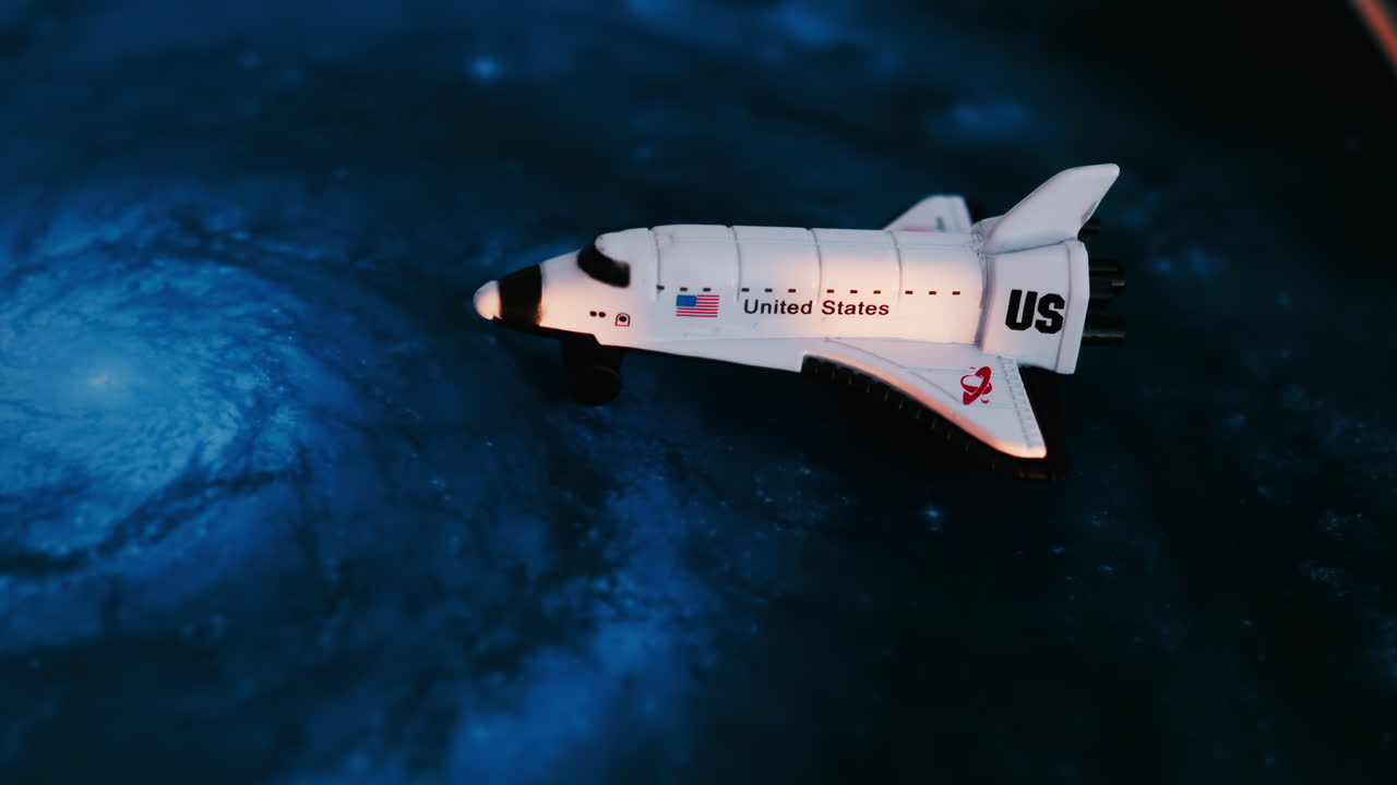 Close up of a miniature toy space shuttle placed on a blue cosmic galaxy backdrop