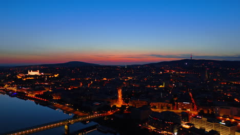 old town in bratislava, slovakia has turned on the street lights. drone footage of the city at night above the danube