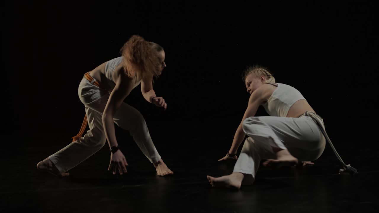 группа профессиональных танцоров практикует капоэйру в темноте под прожектором на черном фоне студии. афро-бразильское боевое искусство, которое сочетает в себе элементы танца.