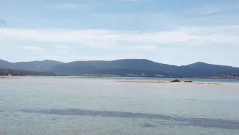 Drone-footage-of-tasmanian-island-beach-flying-fowards-amongst-trees-with-mountains-in-background