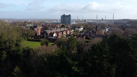 Aerial-view-over-park-trees-to-industrial-townscape-with-Pilkingtons-blue-skyscraper,-Merseyside,-England