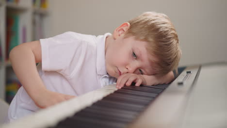 Fatigued-boy-lies-and-presses-random-keys-on-electric-piano