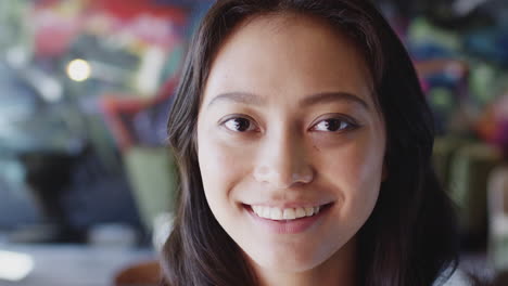 young female asian creative smiling to camera in front of mural in workplace, head shot, close up