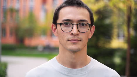 outdoor portrait of a young japanese man wearing eyeglasses smiling and looking at camera