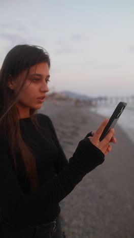 teenager on beach using phone at sunset