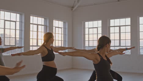 yoga class instructor teaching healthy pregnant women practicing warrior pose enjoying group training exercise in fitness studio at sunrise