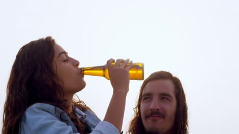 Couple-having-beer-while-sitting-on-car-bonnet-4k