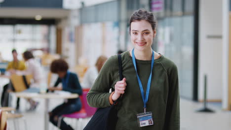 Portrait-Of-Smiling-Female-College-Student-In-Busy-Communal-Campus-Building