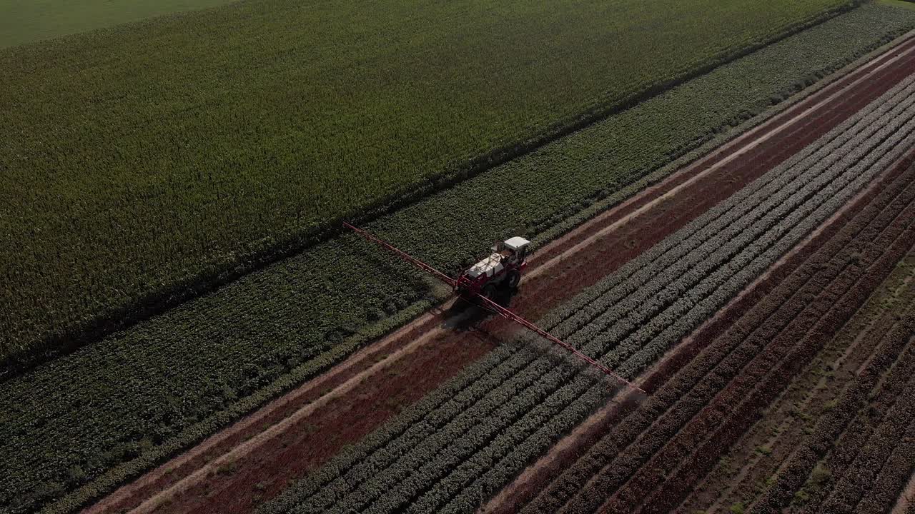 seguimiento aéreo y panorámica detrás de un tractor que arrastra amplios brazos rociadores y una reserva de líquido que se mueve a lo largo de una línea recta de vegetación