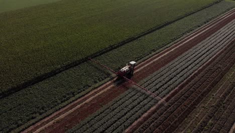 Seguimiento-Aéreo-Y-Panorámica-Detrás-De-Un-Tractor-Que-Arrastra-Amplios-Brazos-Rociadores-Y-Una-Reserva-De-Líquido-Que-Se-Mueve-A-Lo-Largo-De-Una-Línea-Recta-De-Vegetación