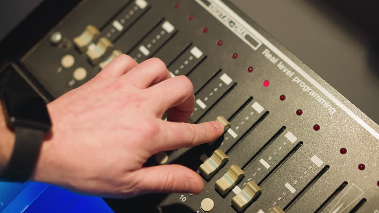 Hand adjusting sliders on digital light controller. Close-up shot of fingers pressing and moving switches, controlling light levels or settings. Working with lighting equipment in studio