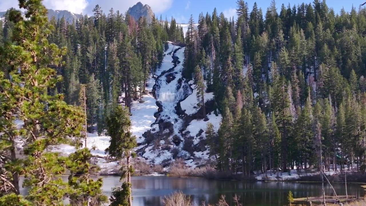 Paesaggio panoramico dei Twin Lakes a Mammoth Lakes, California, con rigogliosi pini verdi, pendii montuosi rocciosi e chiari riflessi sotto la luce del giorno.