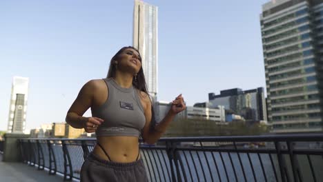 La-Bailarina-Callejera-Mantiene-El-Baile-Mientras-Camina-Hacia-La-Cámara-Con-Confianza-Sonriendo-Estilo-Libre-Sosteniendo-El-Río-De-La-Metrópolis-Del-Carril-Brillante-Día-Soleado-En-Cámara-Lenta