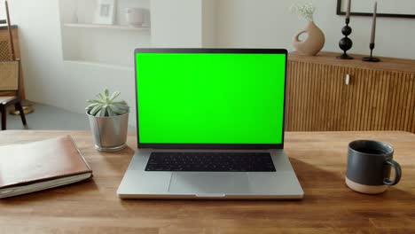 laptop with green screen on wooden table in home office