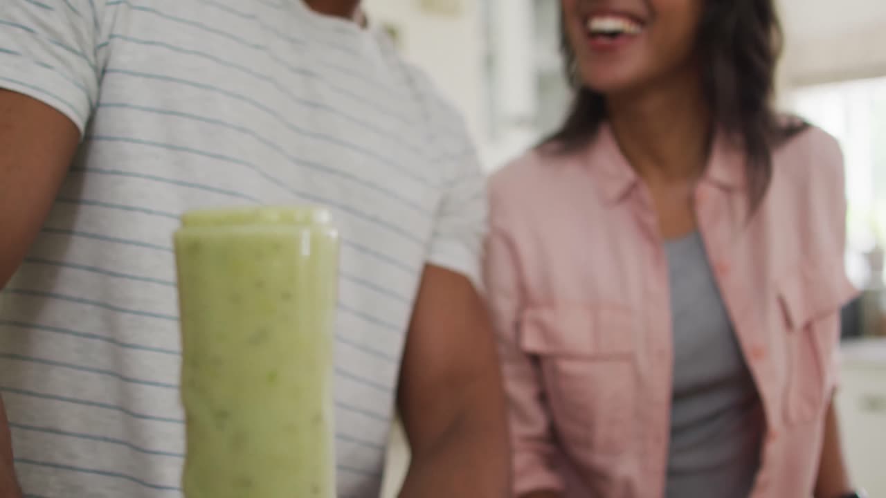primer plano de una feliz pareja biracial en la cocina preparando un batido, usando una licuadora
