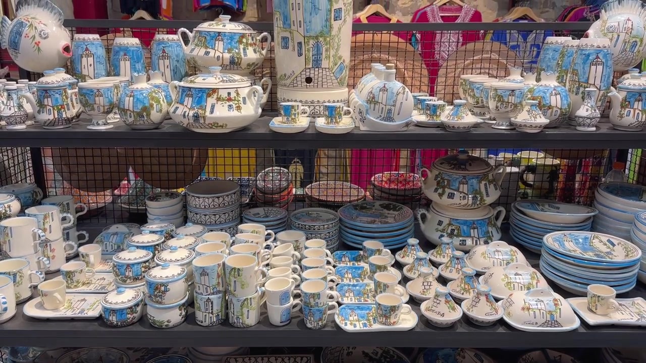 Rows of Tunisian ceramic plates, cups and teapots with blue coastal motifs fill a market stall display, useful for travel, culture or retail themes.