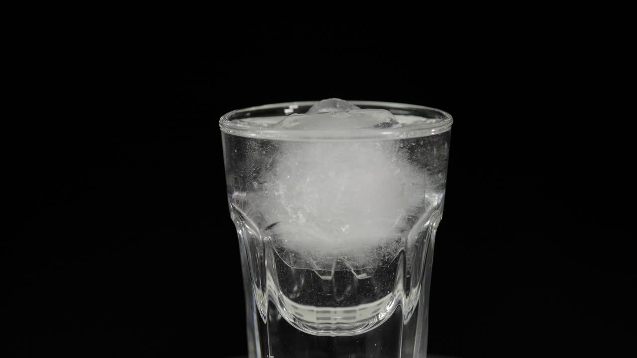 verter vodka en vasos de shot con cubos de hielo colocados sobre un fondo negro