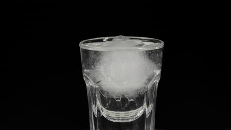 verter vodka en vasos de shot con cubos de hielo colocados sobre un fondo negro