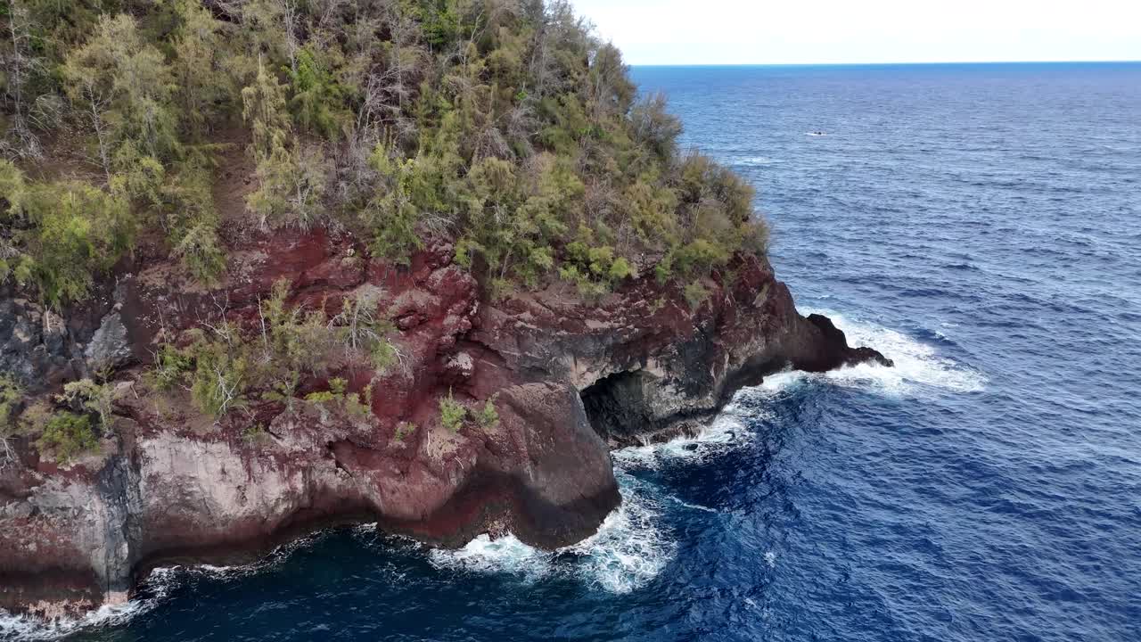 Drone close-up of a wild coastal section in Hana, Maui, Hawaii, featuring rugged rocks and crashing waves. Dramatic tropical shoreline and untouched ocean scenery
