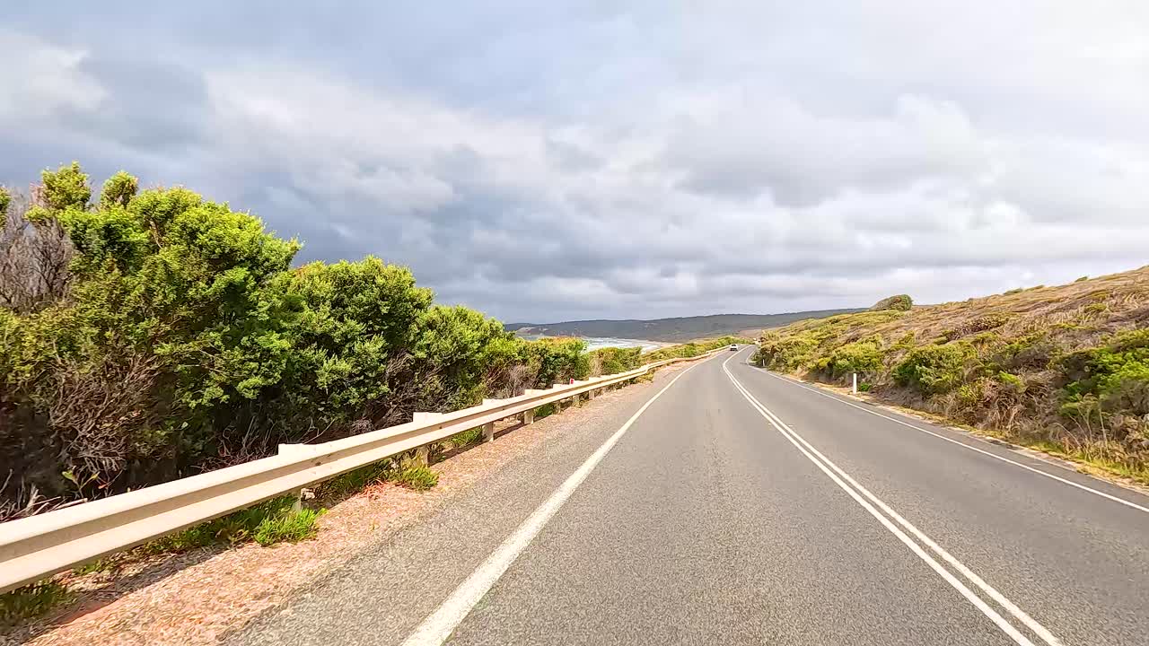 A serene drive along the Great Ocean Road with ocean views, lush greenery, and dynamic skies under natural lighting