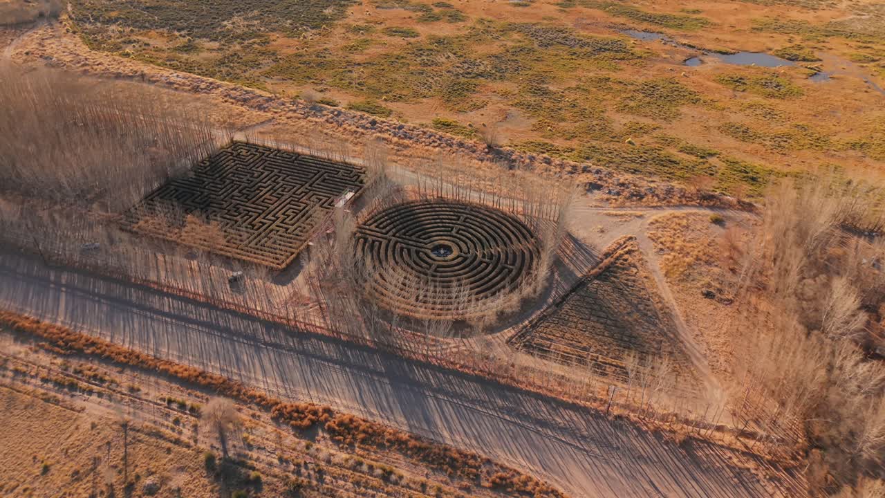 Vista aerea obliqua da drone di due labirinti circolari di siepi affiancati in una campagna aperta e arida in Argentina.