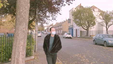 female wearing a medial facemask looking at phone whilst walking on a street towards camera