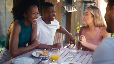 grupo de amigos multiculturales sonrientes desayunando al aire libre en casa mirando el teléfono móvil