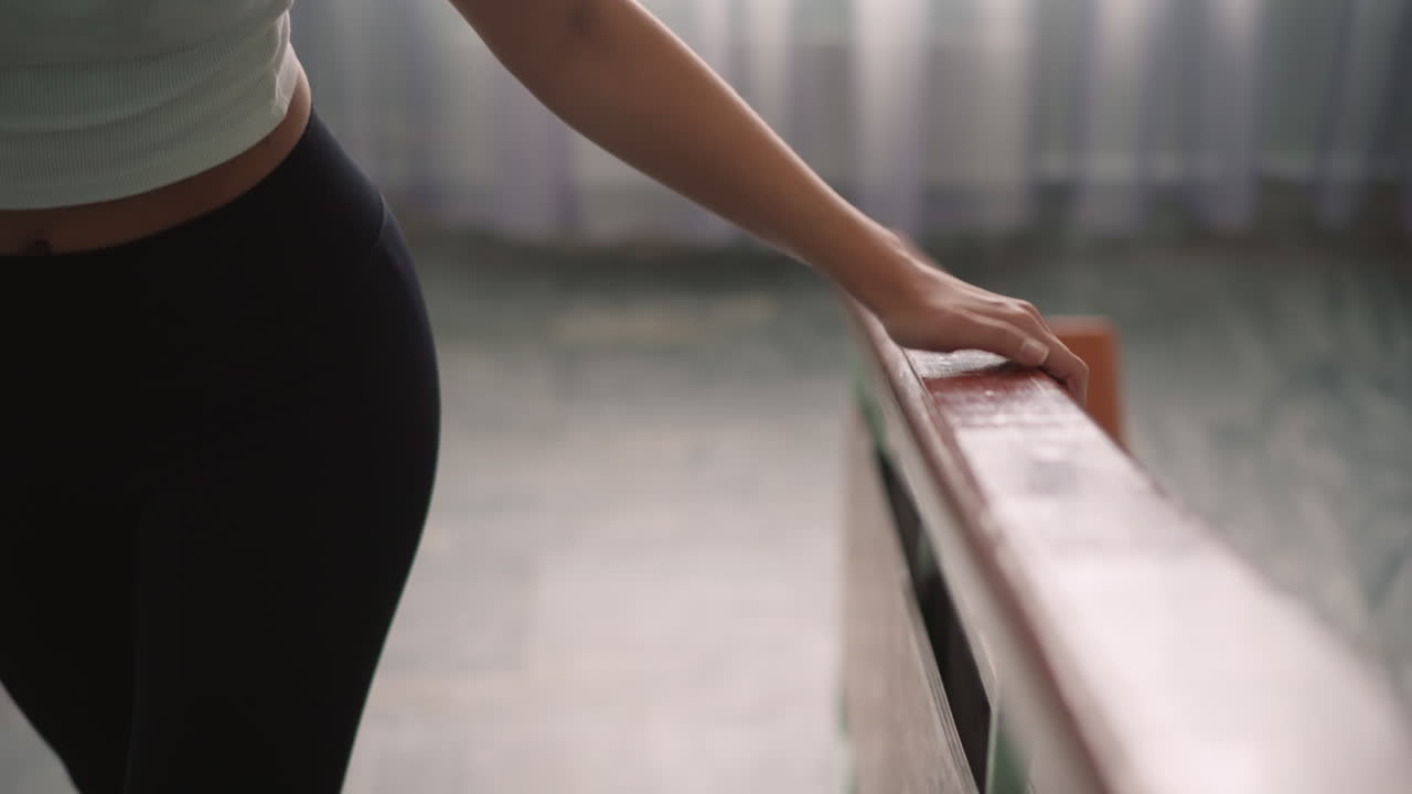 Side view of lady in casual outfit climbing staircase while hand rests on glossy handrail, upward indoor movement symbolizing balance, support, effort, daily activity and calm lifestyle