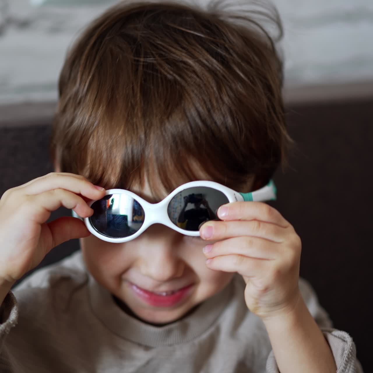 Splendido bambino caucasico con capelli scuri seduto sul divano. Immagine ravvicinata di un bambino piccolo che indossa occhiali da sole.