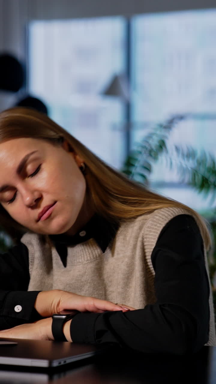 Tired long-haired young woman finished her work on computer. Lady put her head on the elbows and closes eyes to have some rest. Vertical video