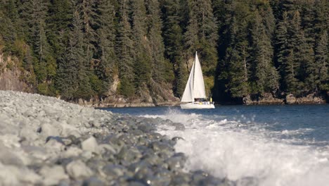 Wellen-Schlagen-Gegen-Die-Felsige-Küste,-Während-Ein-Schiff-Auf-Dem-Blauen-Ozean-In-Einem-Dichten-Waldberg-In-Alaska,-USA,-Fährt