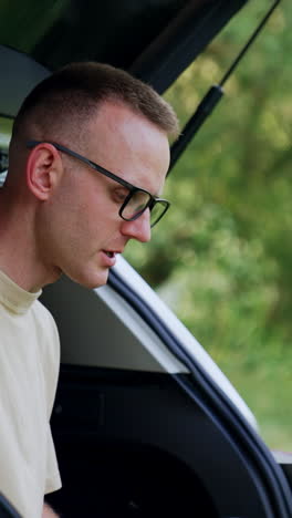 Working in nature. Man in glasses types on his laptop, speaking to himself. Freelance concept. Vertical video