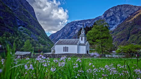 Landscape-of-a-building,-picturesque-house-in-a-flower-field-between-mountains-and-moving-clouds-in-the-sky