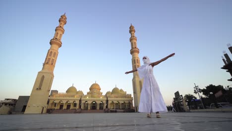 puesta de sol, amanecer vista de la mezquita de el mina con mujer turista en largo vestido blanco y hijab girando y disfrutando de la vista de la mesquita