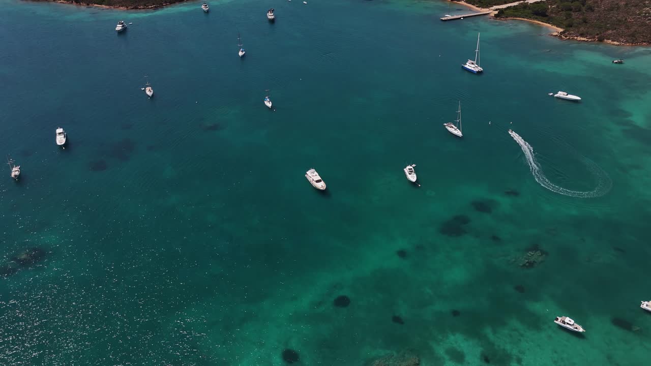 Yachts drift in Sardinia's turquoise waters under a sunny sky