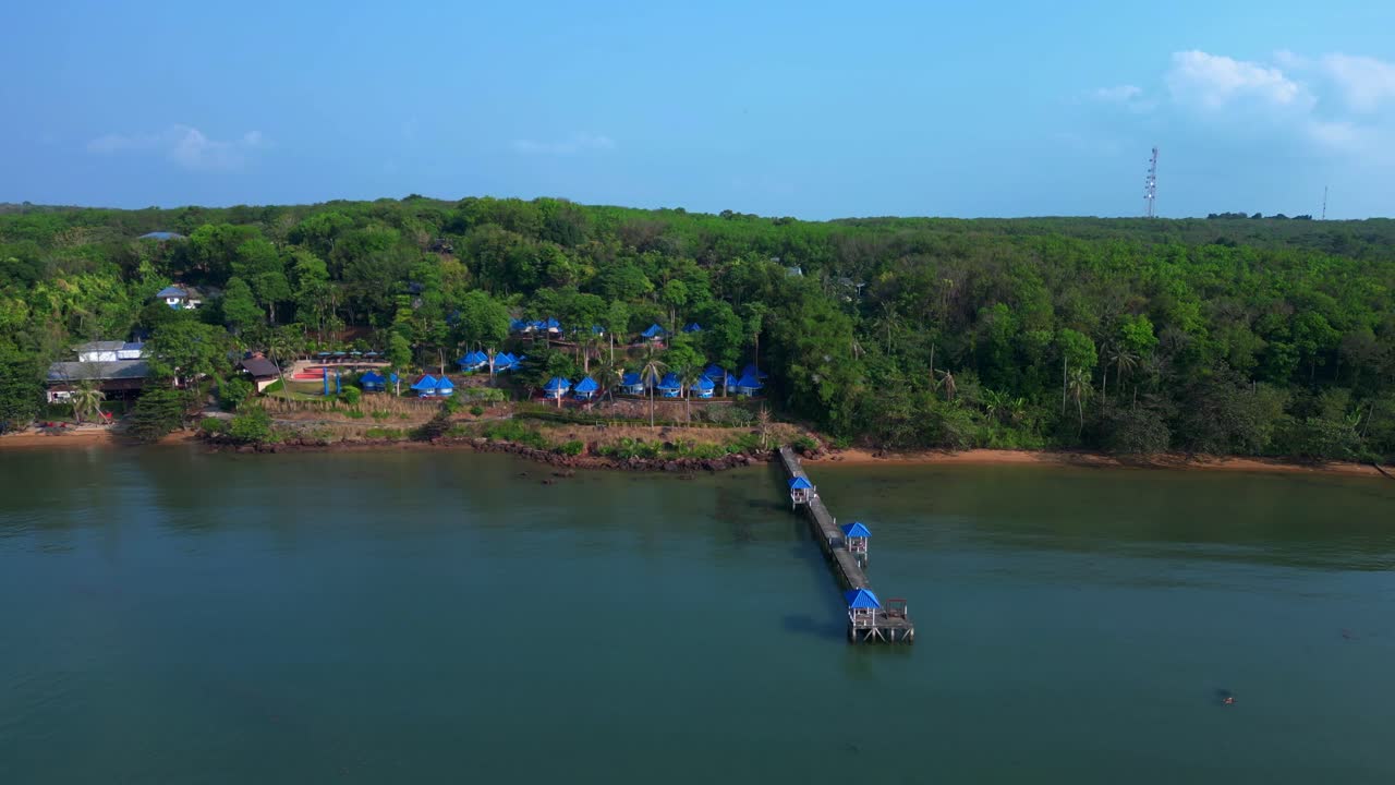 Koh Mak tropical island in Thailand showing luxury glamping tents on the coast near the pier surrounded by lush vegetation. Stunning aerial view flight static tripod hovering drone