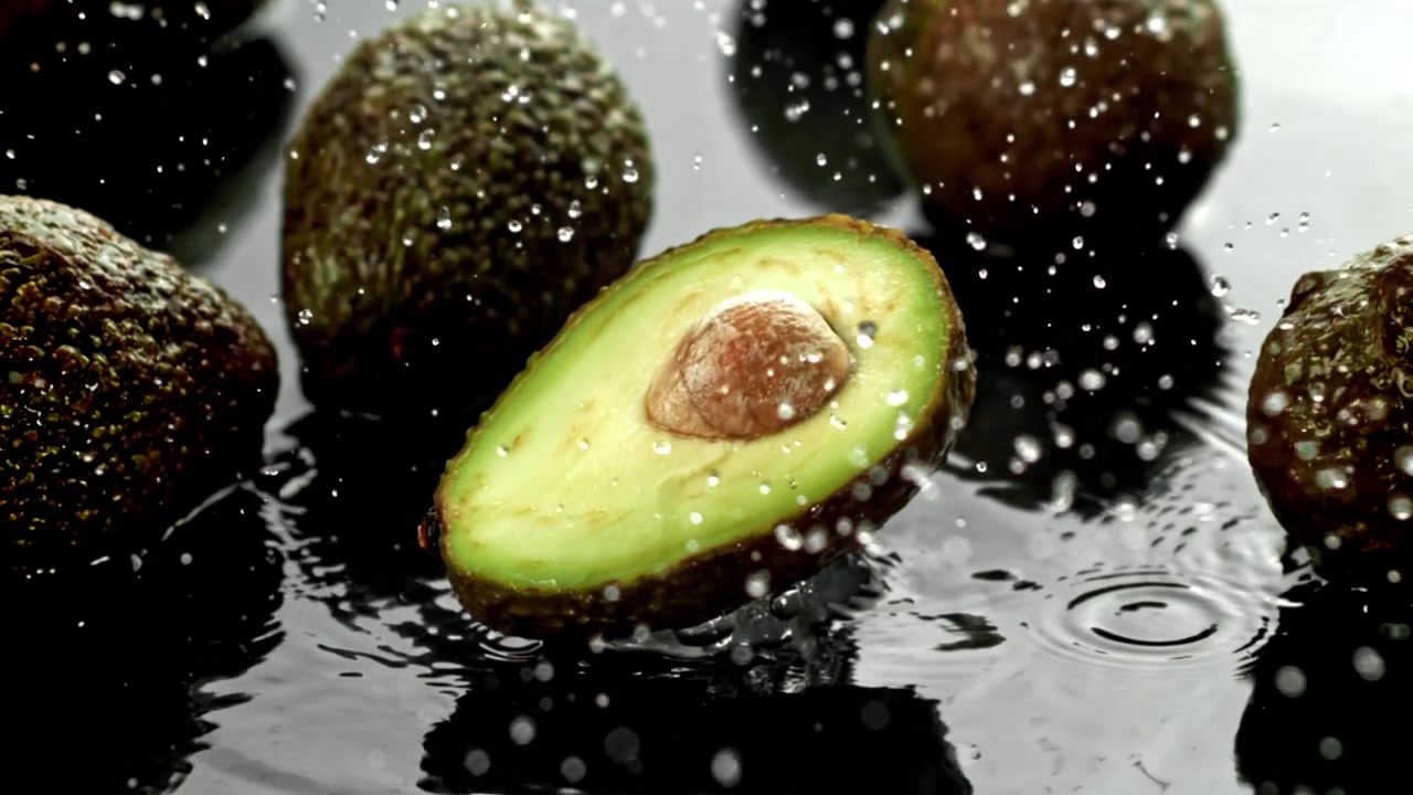 Mezzo avocado fresco con schizzi d'acqua su sfondo nero