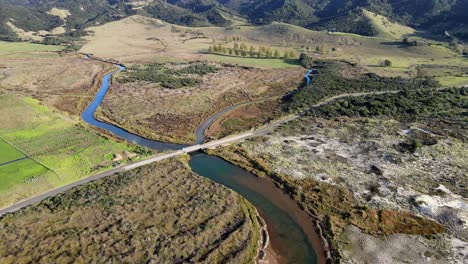 cars crossing small bridge across the river, aerial reveal of panoramic scenery, forested hills and beach