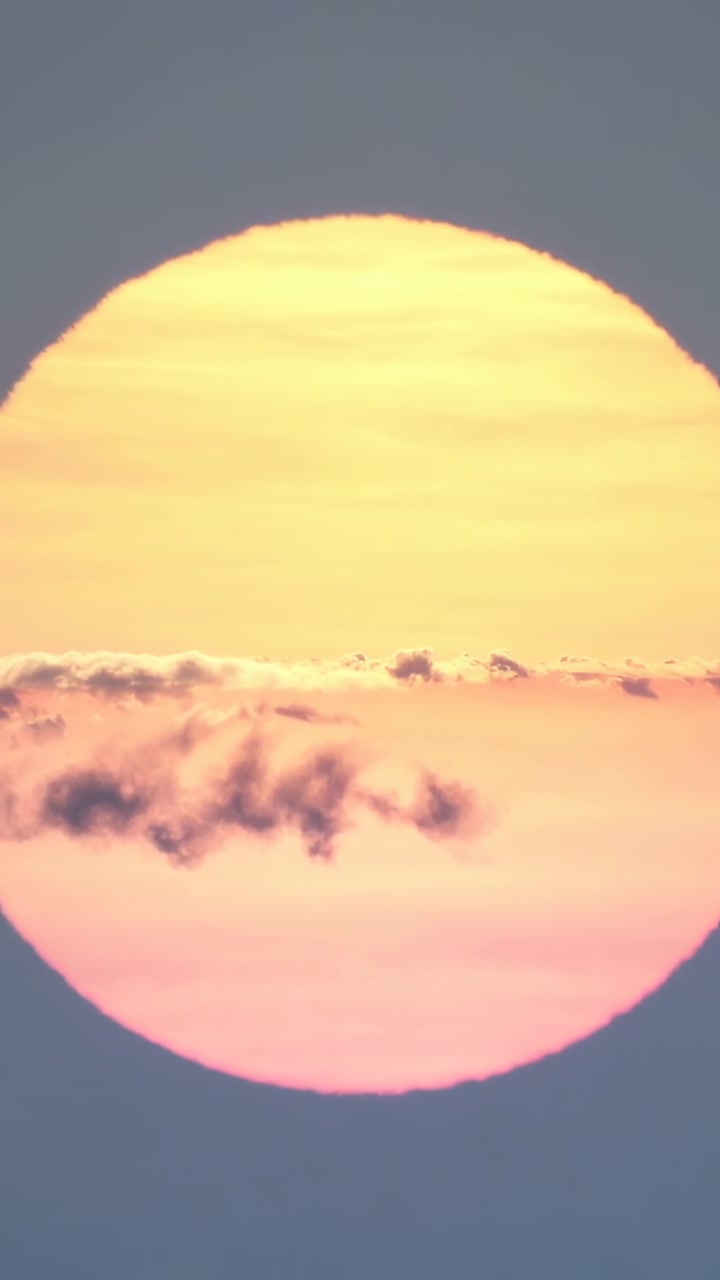 Vertical video: Revealing centered sun shifting hues near horizon, with low cloud bank drifting