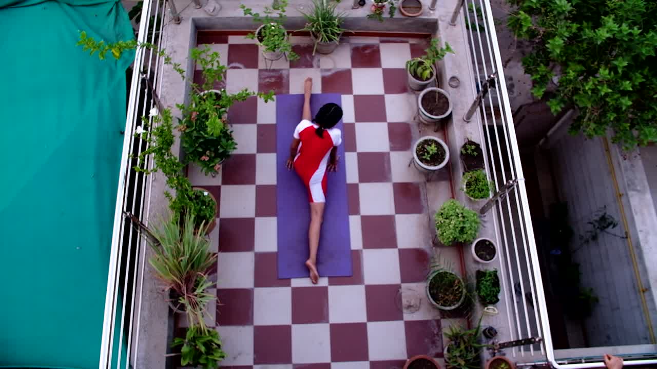 escena de ángulo superior de una joven india haciendo yoga y pranayama en su jardín de terraza rodeada de plantas de hermosas flores que le dan energía
