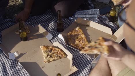 closeup shot of friends eating pizza in park