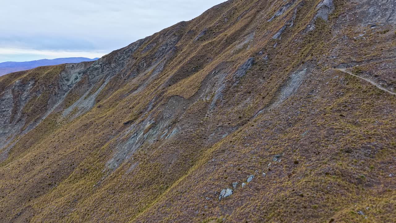 Drone flying forward along the mountain slope of Roys Peak in Wanaka, revealing winding trail paths and rugged terrain