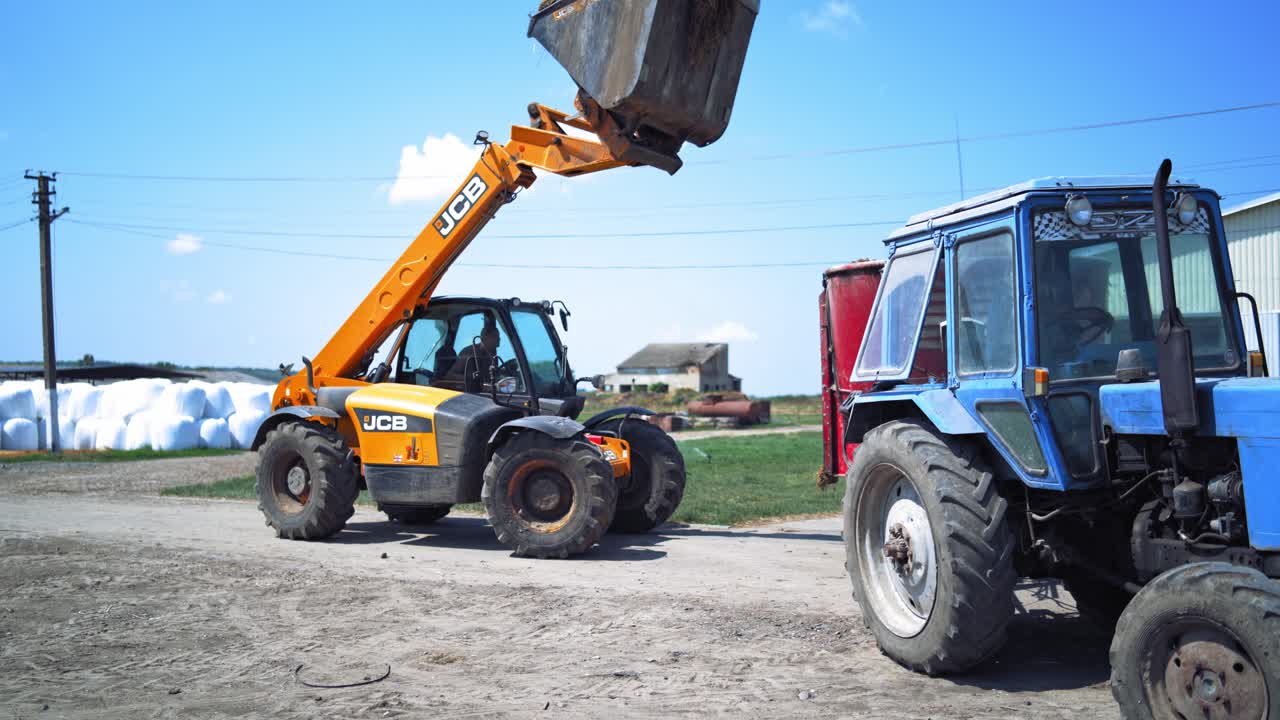 Agricultural machinery on farm. Tractor loads bales of hay on trailer