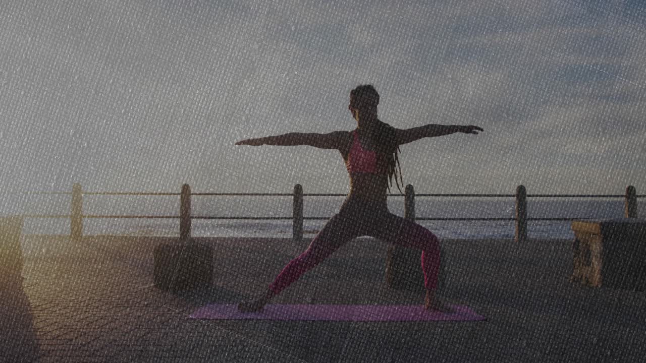 Alba che ispira un istruttore di yoga in posizione del guerriero II su una terrazza sull'oceano, attivando il core e spostando lo sguardo.