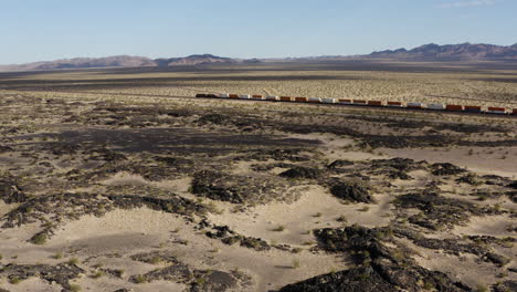 extremely long freight train speeds quickly down a completely straight train track through a desert landscape