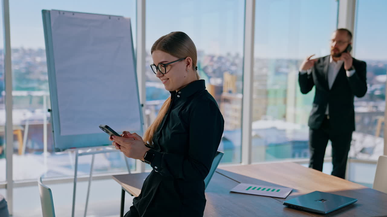 Business people in office. Pretty woman and elegant man wearing a black suits use phones in their work. City panoramic window view.