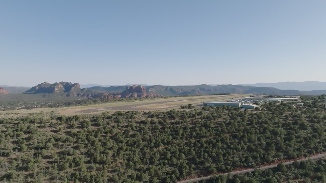 el aeropuerto de sedona y el paisaje verde con formaciones rocosas rojas distantes bajo cielos azules claros, vista aérea