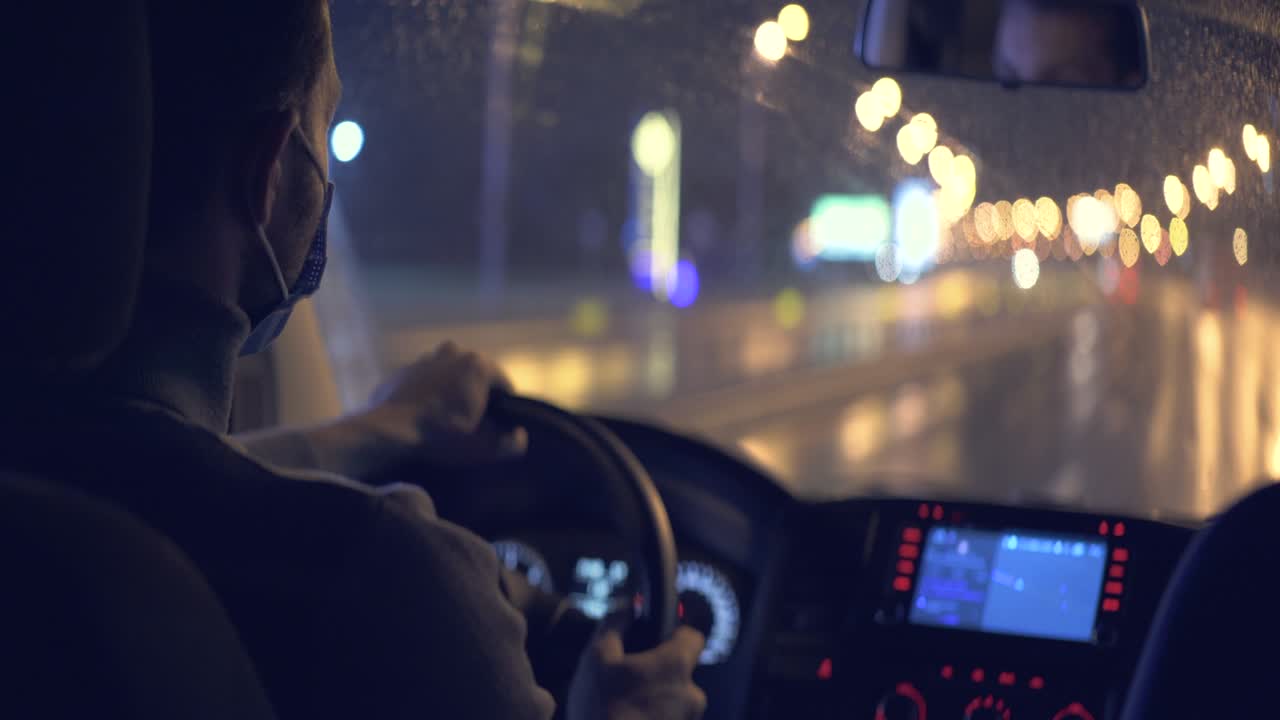 el hombre con una máscara médica conduce a través de la carretera de la ciudad nocturna.